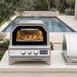 Blaze oven with pizza inside beside a grill, with a pool in the background