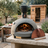 Piko oven cooking pizza with a cedar sauna in the background